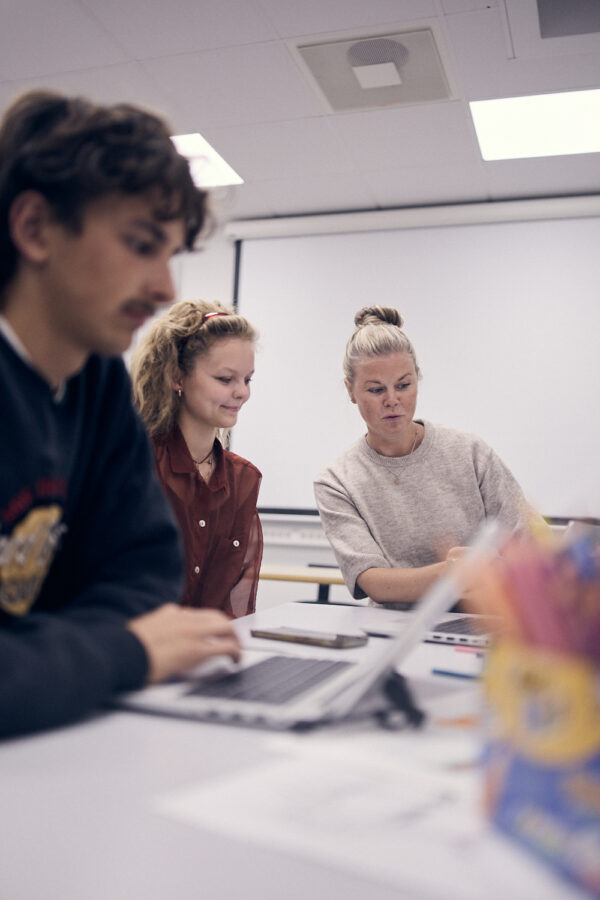 En lärare sitter tillsammans med två elever och går igenom skoluppgifter.