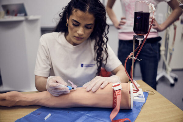 En elev demonstrerar hur man ska ta ett blodprov på en docka i klassrummet.