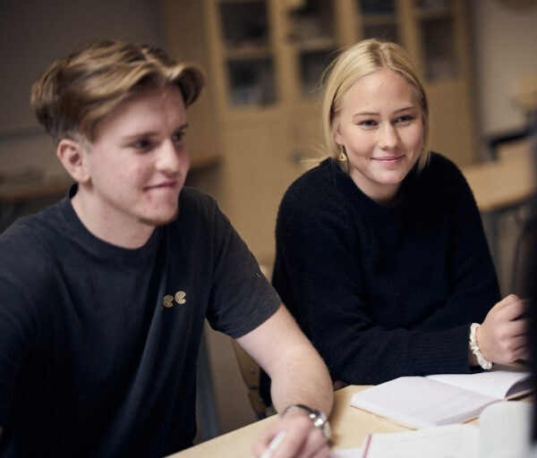 Två elever sitter vid ett bord och lyssnar på en genomgång i klassrummet