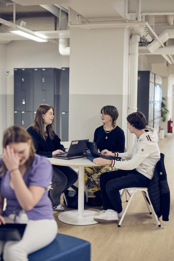 Elever samarbetar och arbetar med laptops i studie- och uppehållsutrymme på en skola.