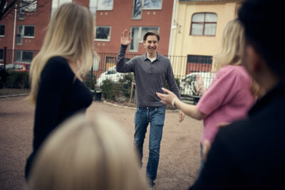 En leende gymnasieelev vinkar tillbaka när han närmar sig en grupp klasskamrater som hälsar honom välkommen.